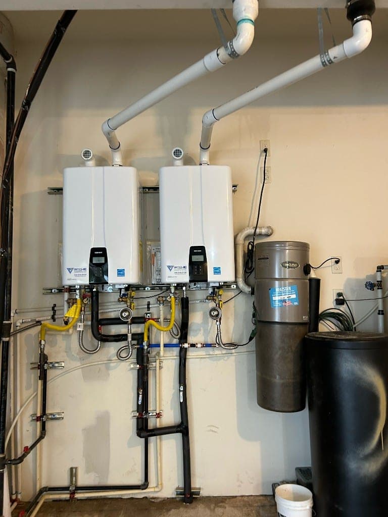 Two Navien tankless water heaters mounted side by side with Ritchie Plumbing labels, gas, and PVC venting