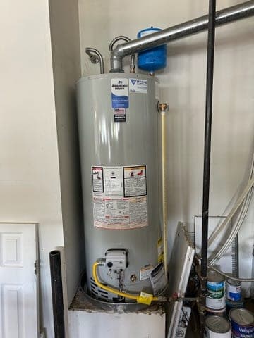 Bradford White tank water heater with a Ritchie Plumbing service sticker, blue expansion tank, drain pan, and yellow gas line