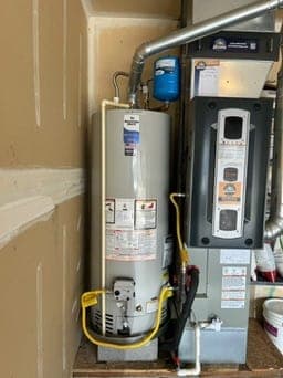 Gas tank water heater set beside a furnace with expansion tank, metal flue, drain pan, and insulated lines